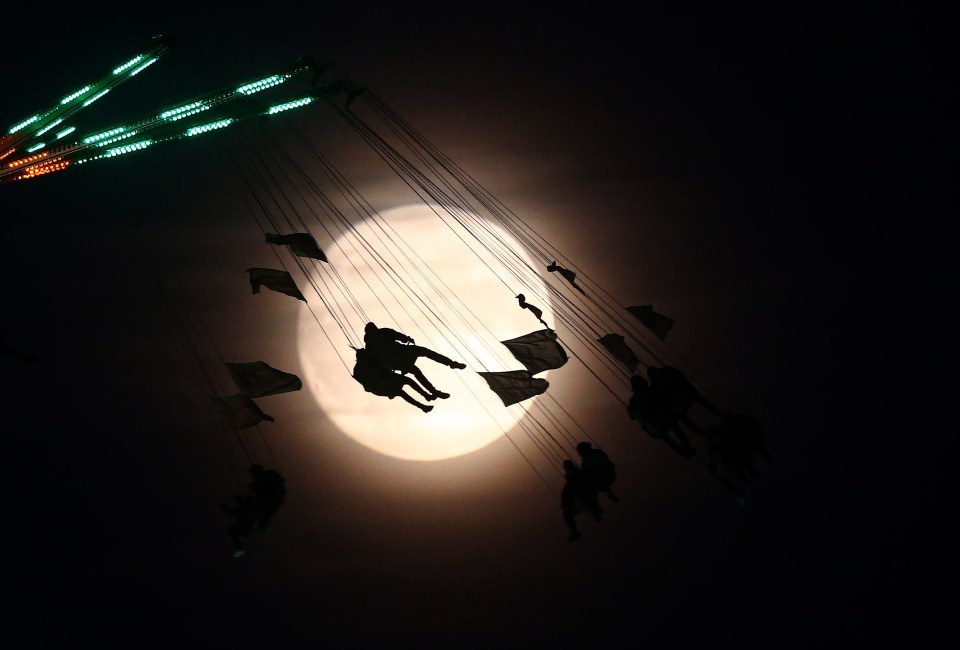 Riders on a funfair attraction in London are captured in a spectacular silhouette against the shining full moon