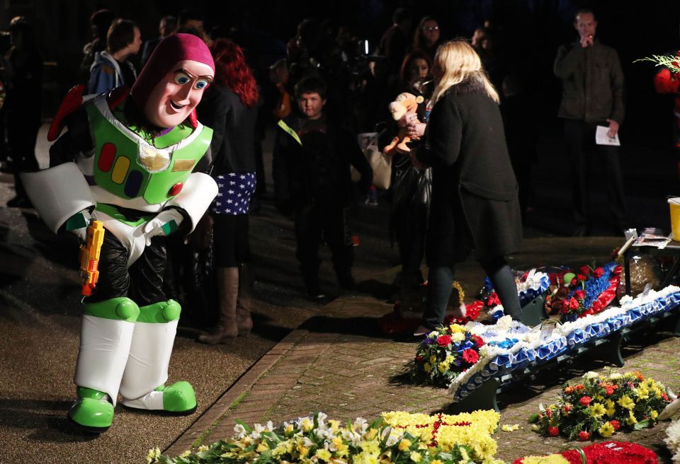A mourner dressed as Buzz Lightyear looks at floral tributes during the funeral of 18-year-old Arthur Peebles
