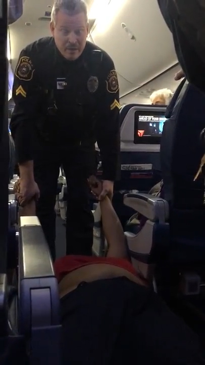 The woman can be seen being pulled down the aisle by her arms as shocked passengers looked on