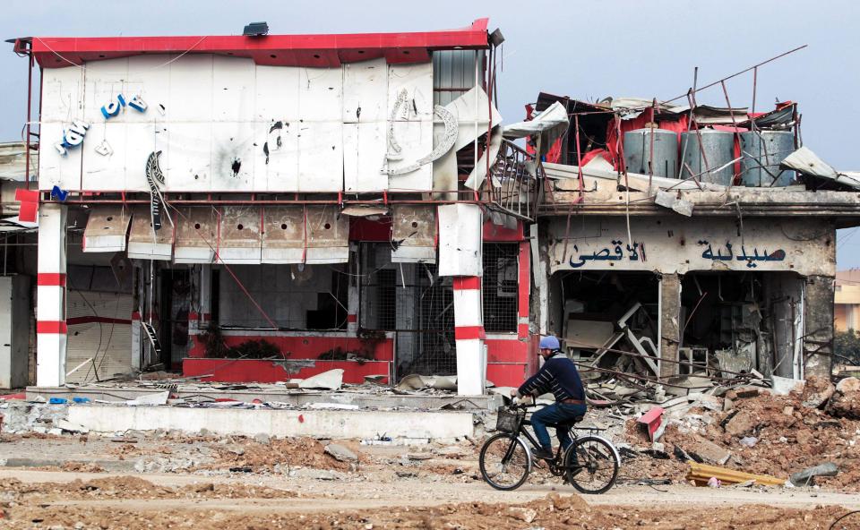 An Iraqi man cycles past damaged buildings near the University of Mosul after its liberation