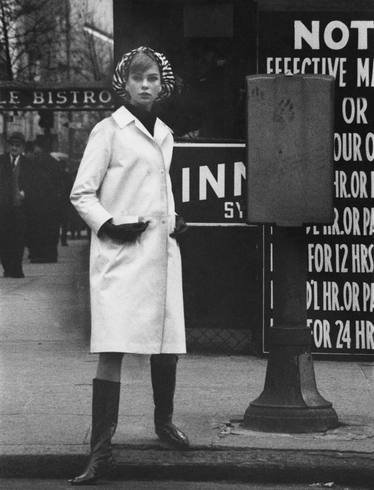  A model is photographed while wandering down the street in a chic white coat and knee-length patent boots (David Bailey, American Vogue, April 1962 © 1962 Condé Nast)