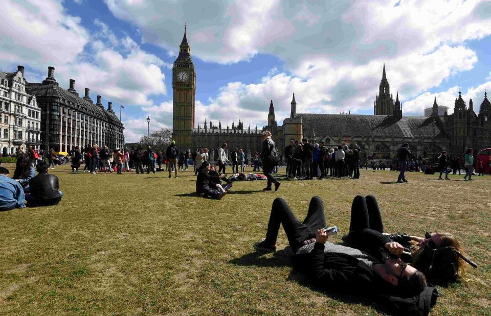  Tourists relax in the sunshine on Parliament Square opposite the House of Commons today