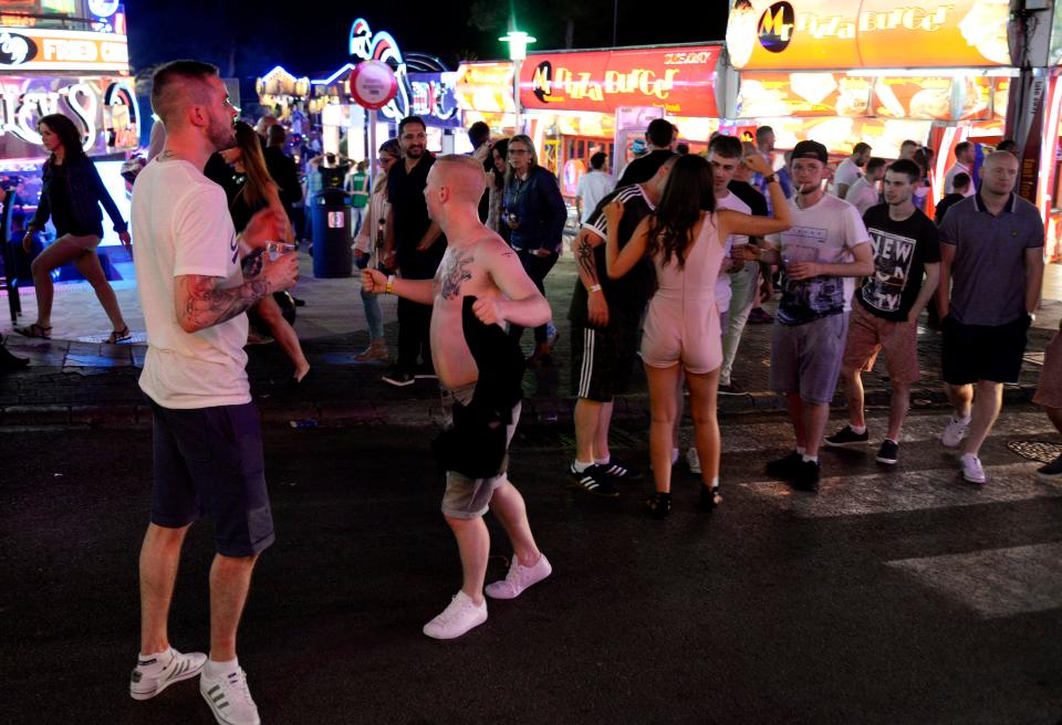  A shirtless man and a group of friends chat with a woman as they enjoy a night out in the Spanish party town
