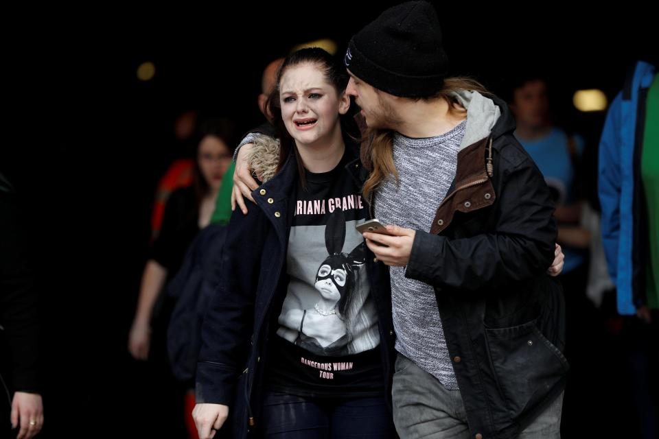 A young woman in an Ariana Grande shirt is comforted as she flees the centre