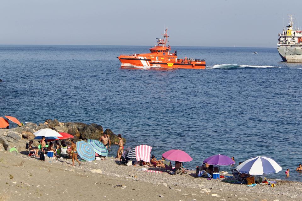 Spanish coastguard bring migrants just rescued off the North African coast past holidaymakers