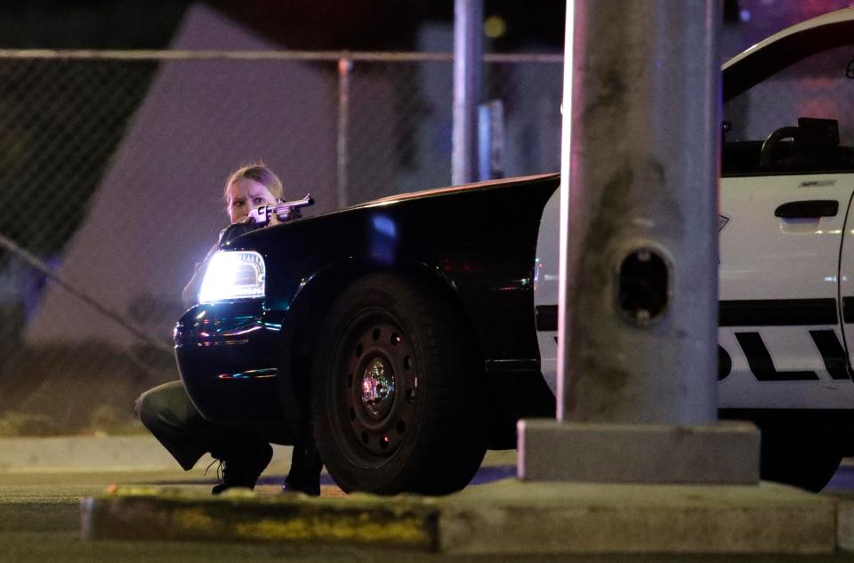 An officer crouches down for cover, armed with a gun