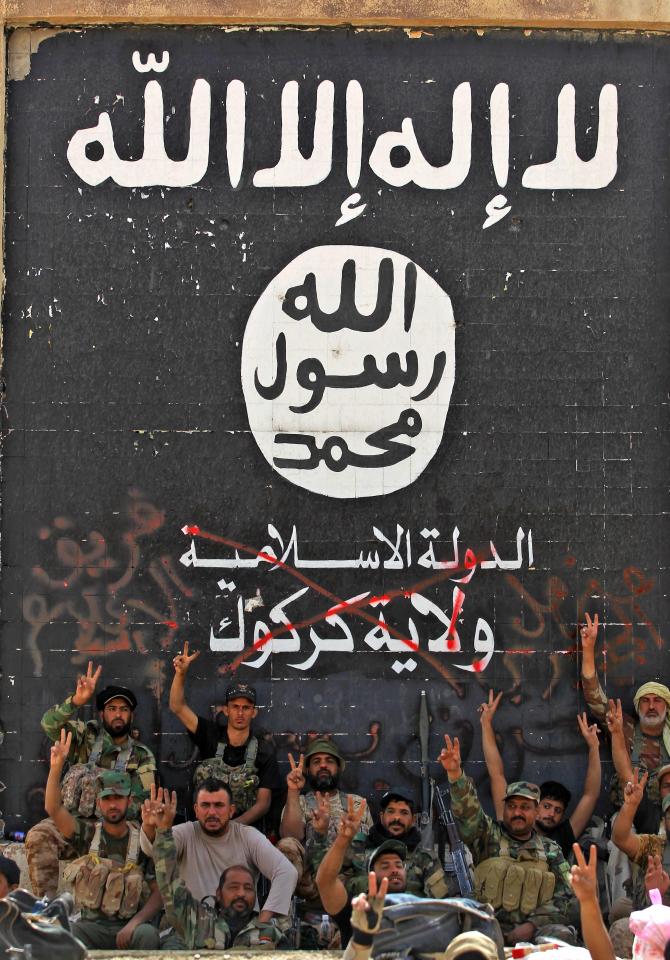  Iraqi forces, pose in front of the black ISIS flag after retaking the town