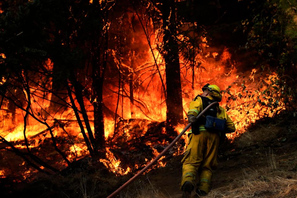  A firefighter carries a water hose to put out a fire during along the Highway 29 near Calistoga, California