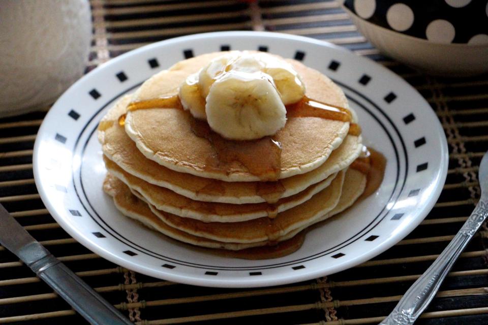 Stack of pancakes topped with banana slices and syrup on a plate.