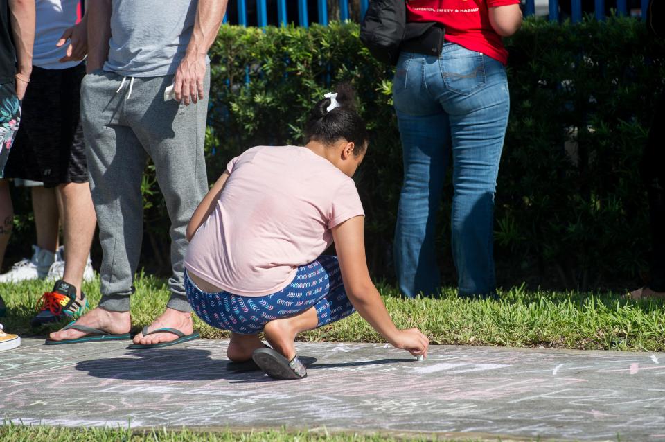  A woman crouches down to write on the pavement in chalk as many left tributes to the rapper