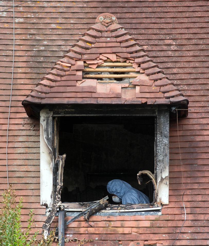 An officer is glimpsed through the scorched windows of the semi-detached home
