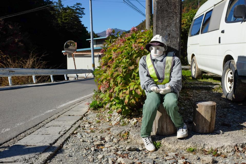  A doll wearing a construction outfit sits on a stool outside the driveway