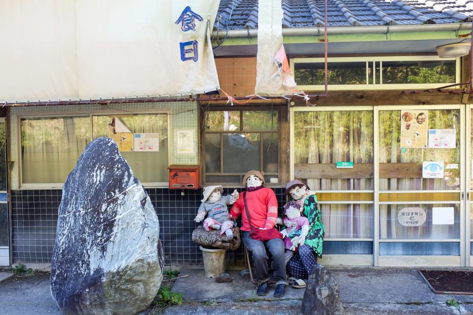  Two adult dolls and two child-like dolls sit outside a building