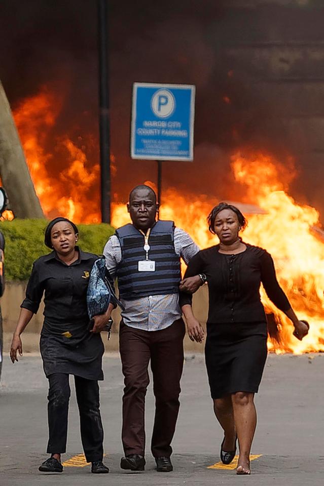  A security member escorts two women to safety as cars burn in the background