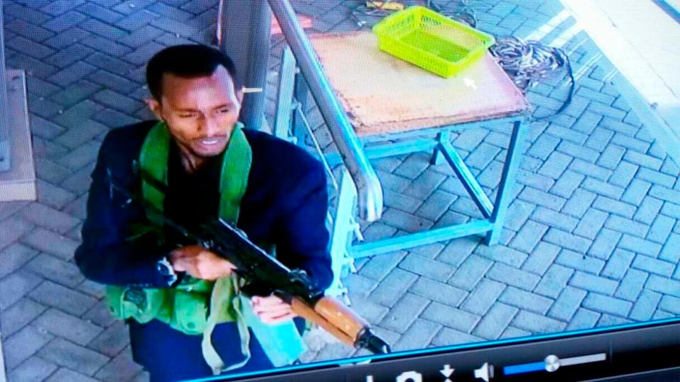 An alleged attacker, holding an automatic weapon and wearing an ammo belt, enters the hotel