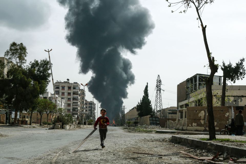  A child runs in front of clouds of smoke billowing following a strike on Douma