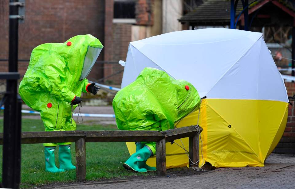 Members of the emergency services in green biohazard encapsulated suits investigate the bench where they were found in Salisbury