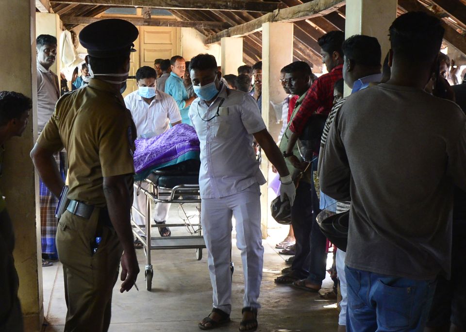  Sri Lankan hospital workers transport a body on a trolley at a hospital morgue as sombre people look on