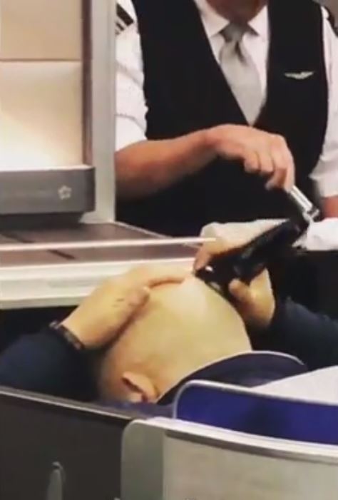 A flight attendant walks past while the man is using the electric razor