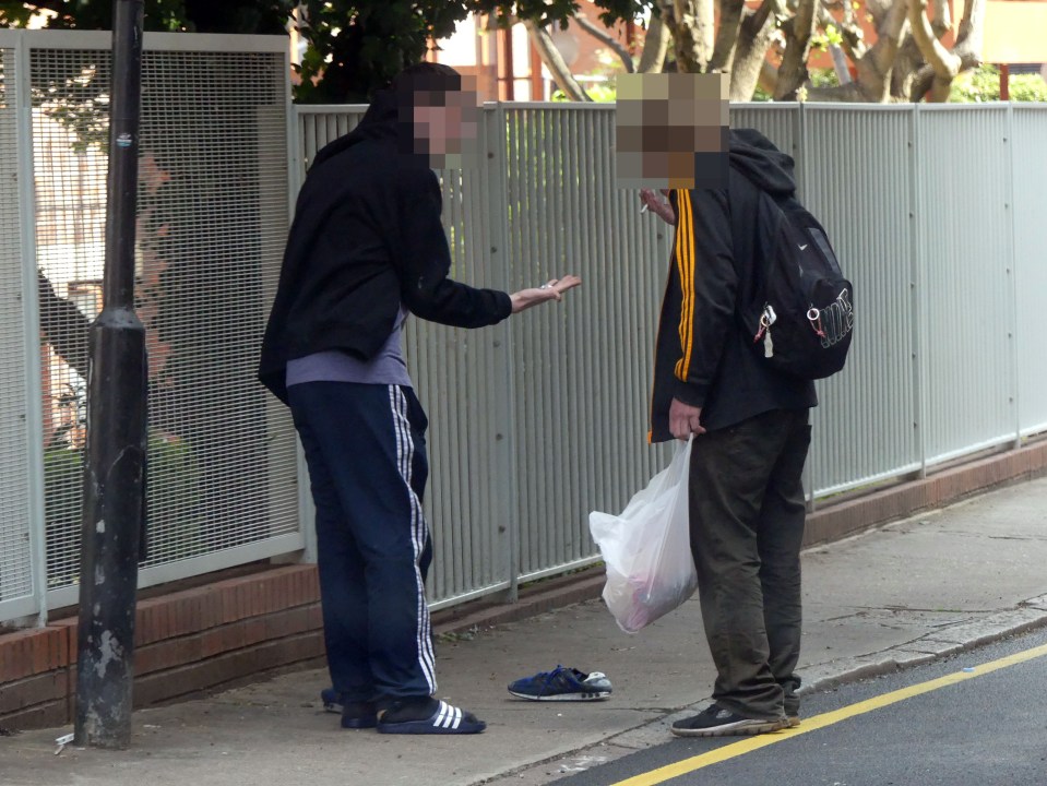 A man in tracksuit bottoms holds open his hand to show small, white rocks while on Batty Street in broad daylight