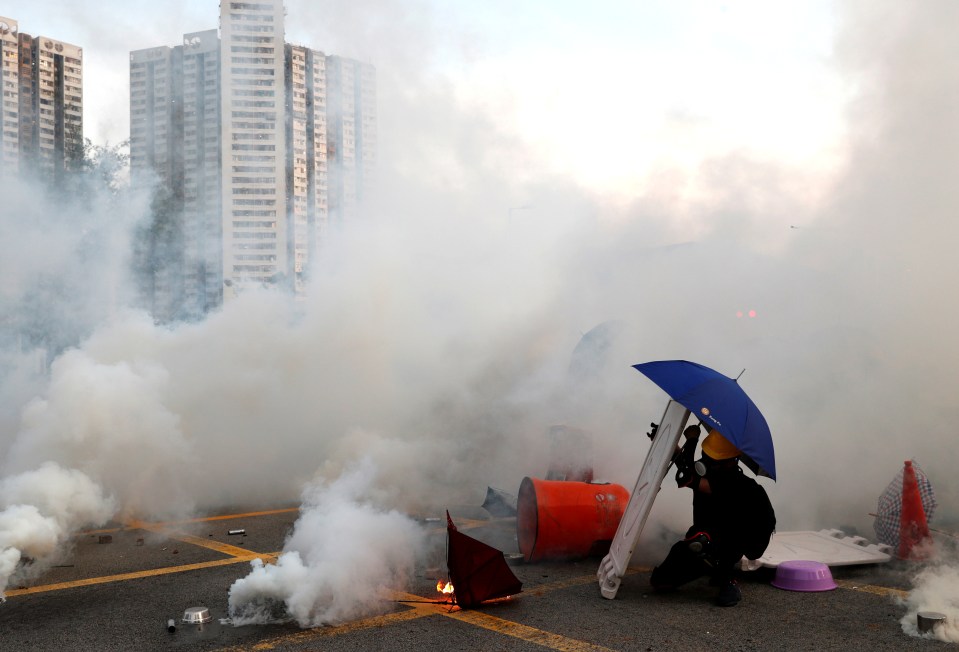 A protester wearing black holds up an umbrella against tear gas