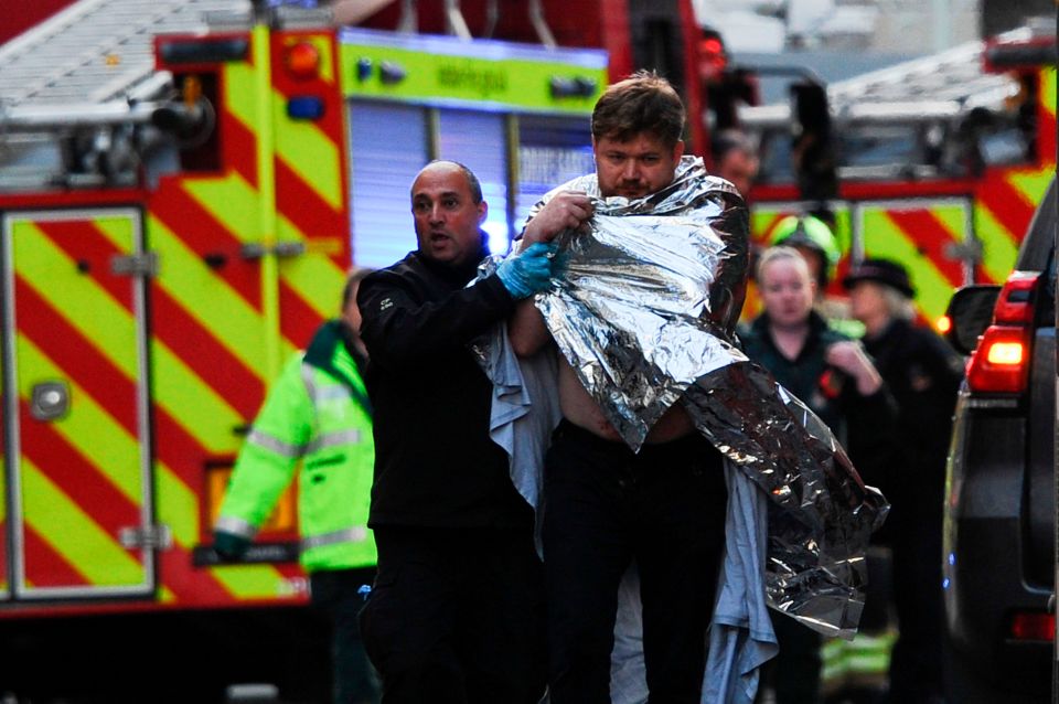 A man is bundled away from the scene wrapped in a blanket 