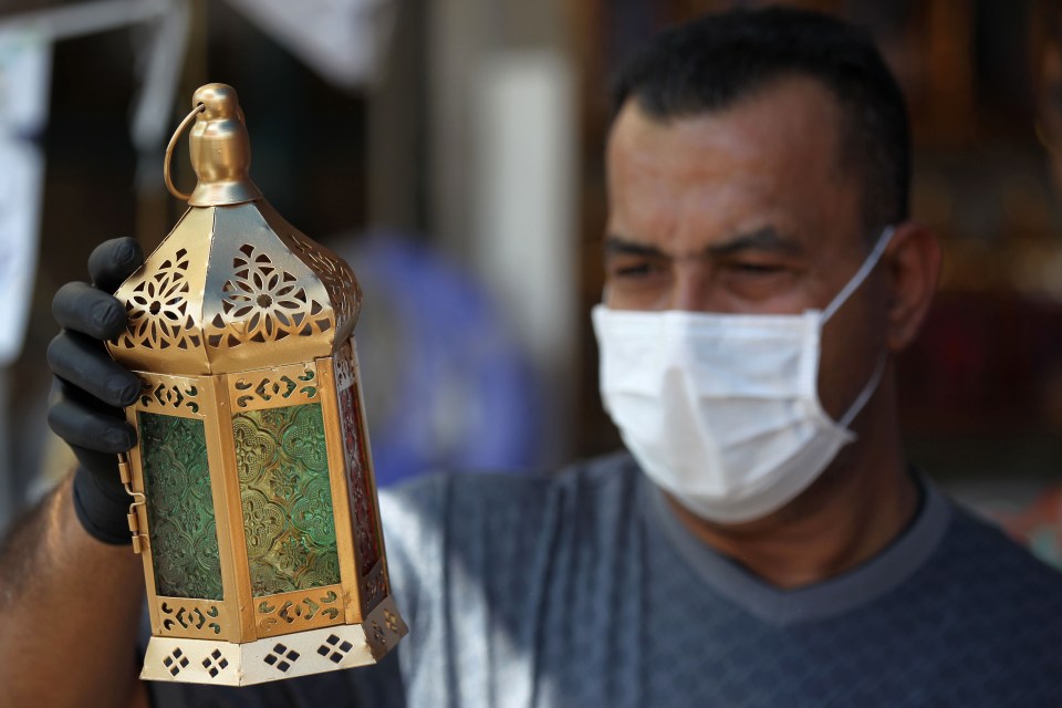 An Iraqi man wearing plastic gloves and a protective mask holds a traditional 'Fanous' lantern