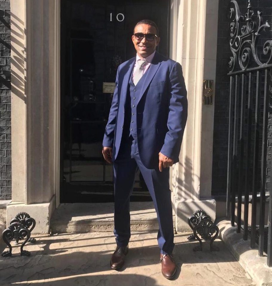 a man in a suit stands in front of a building with the number 10 on it