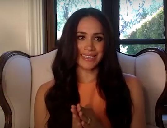 Meghan was sitting in a vintage-looking, cream armchair which had mahogany-style wood framing