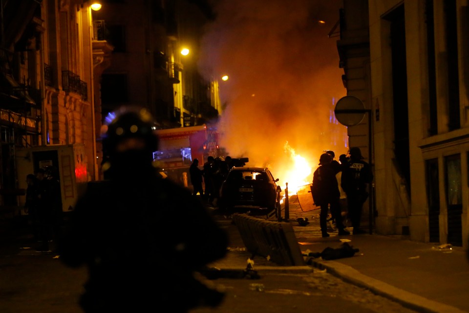 French police officers watch a car burning near the Champs-Elysee