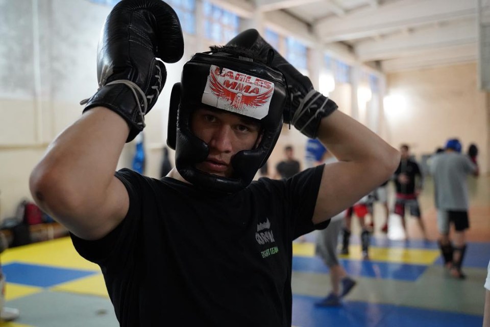 Usman Nurmagomedov putting on boxing gloves and headgear.