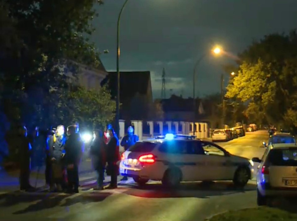 A camera crew films on as police cars guard the scene