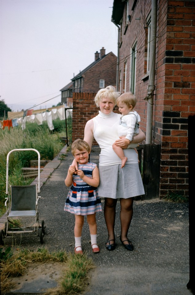 A mother and her two young children stand outside their home in England in 1963 as washing dries in the background 
