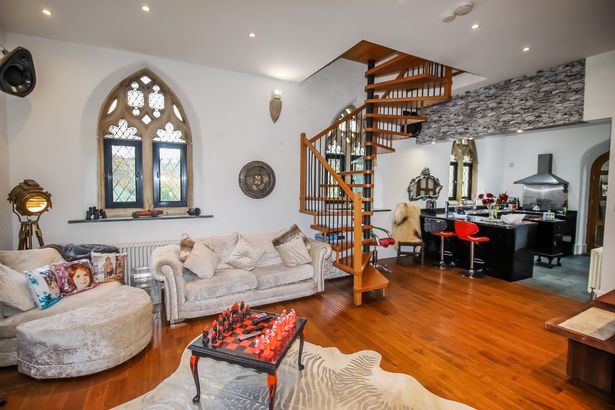 A modern living room with a a kitchen island is shown with aspects of the old chapel still remaining 