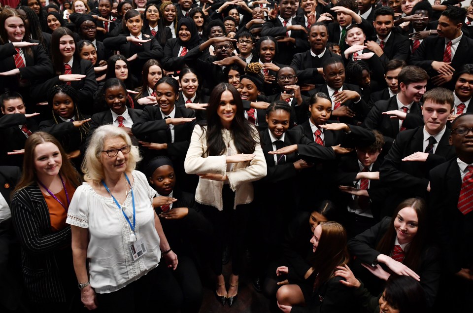 Meghan poses with school children making the 'Equality' sign during a visit to Robert Clark School in Dagenham 
