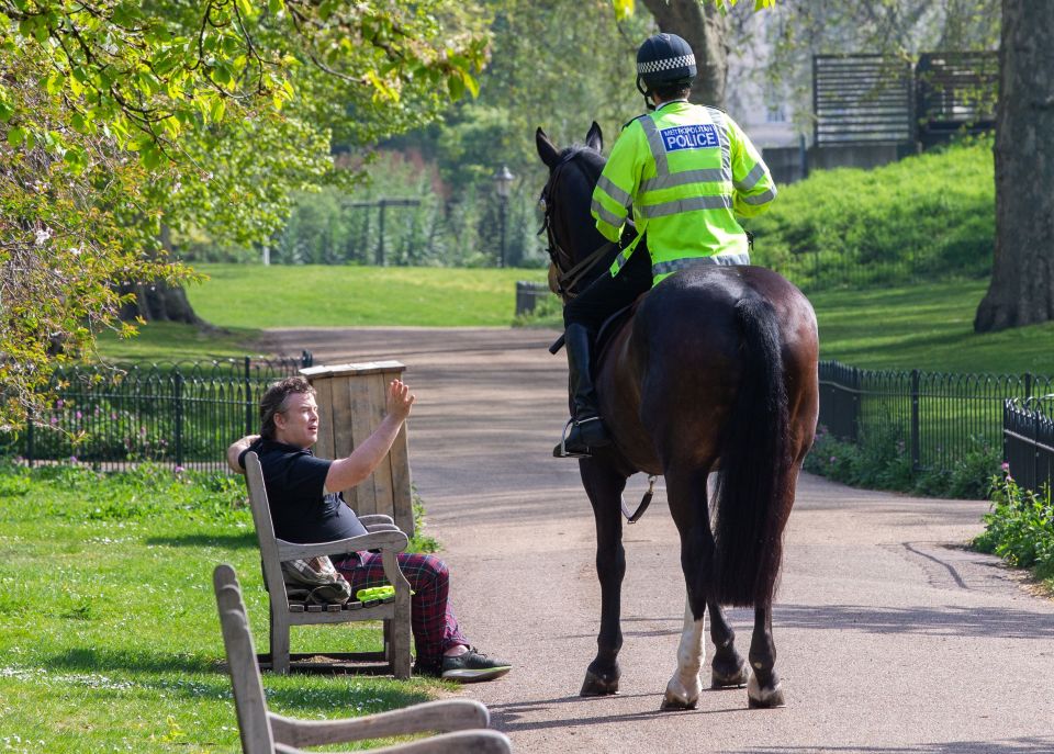A police officer speaks to a member of the public sitting on a park bench in London in May