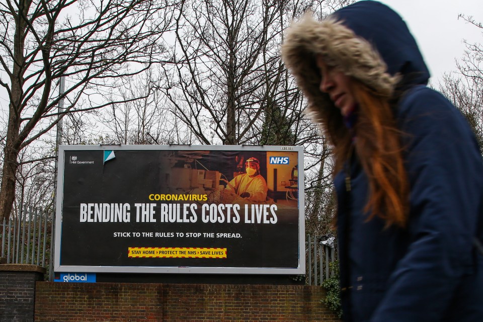A woman walks past the government's "bending the rules costs lives" awareness publicity campaign poster in north London. Testing will be ramped up in Tottenham 