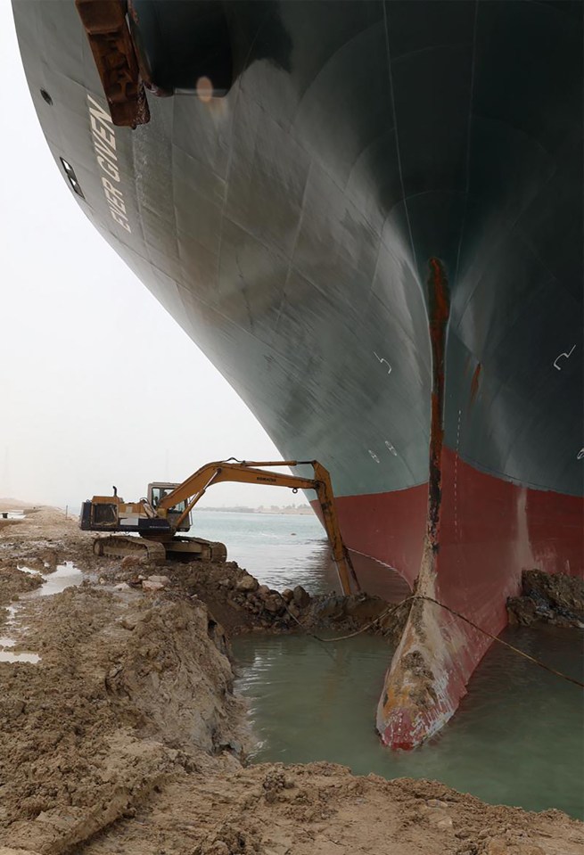 A digger working to free the ship from the side of the canal
