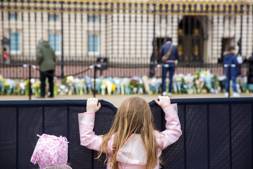 A young girl peers over the barrier to see floral tributes left in the Duke's memory