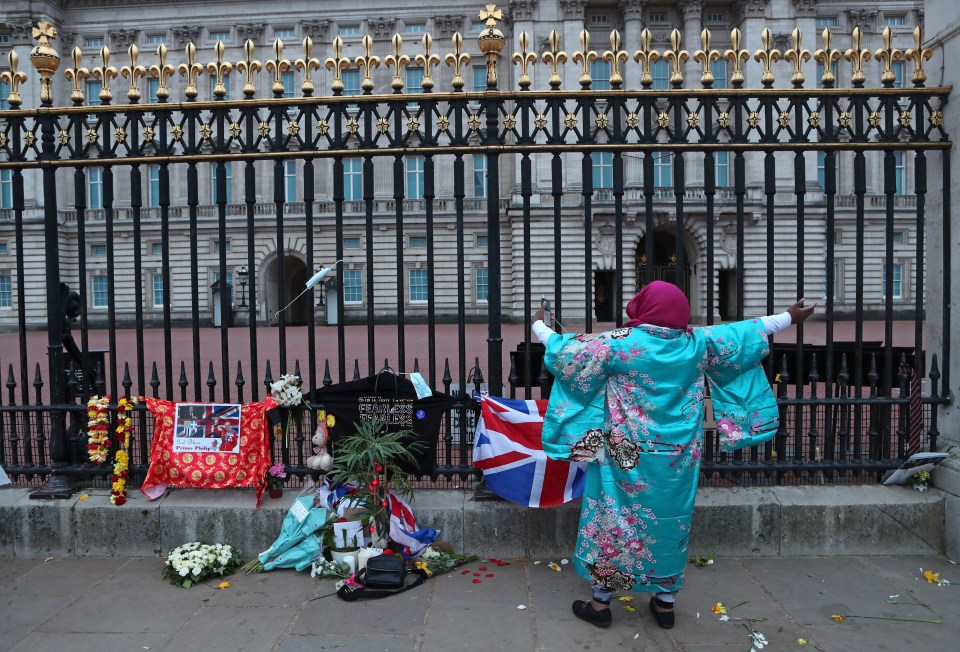 A woman gestures as she sings next to tributes in front of Buckingham Palace
