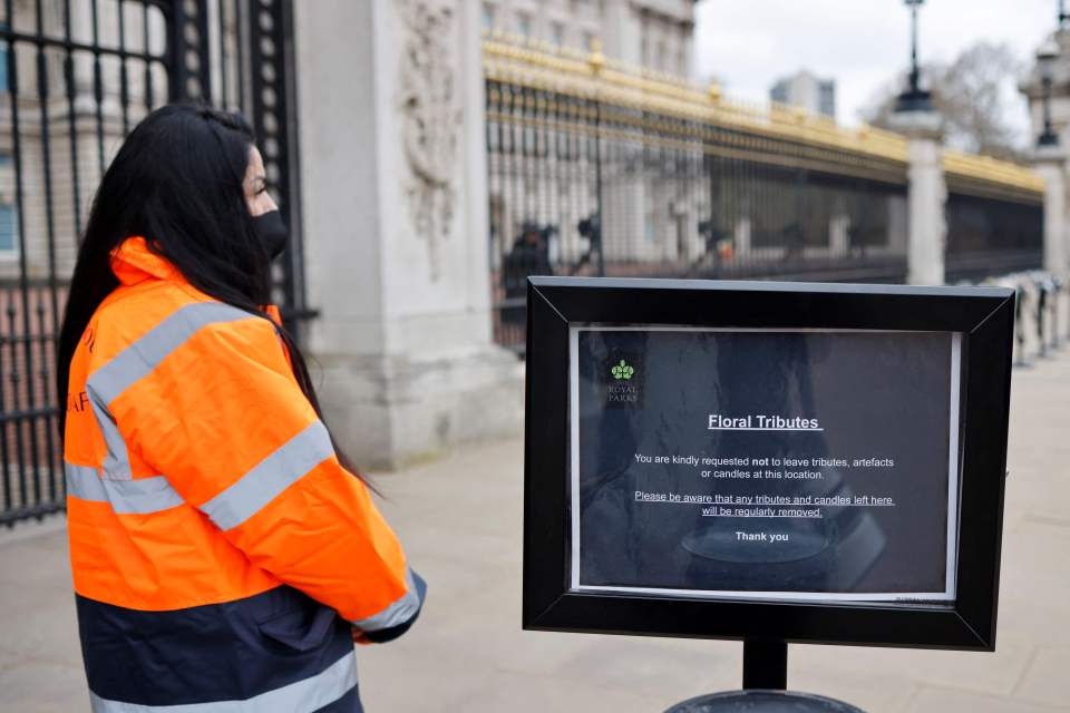 A security official stands alongside a sign requesting the public not to leave floral and other tributes to the Duke of Edinburgh outside Buckingham Palace