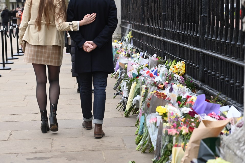 People lay flowers and walk past the fence outside Buckingham Palace