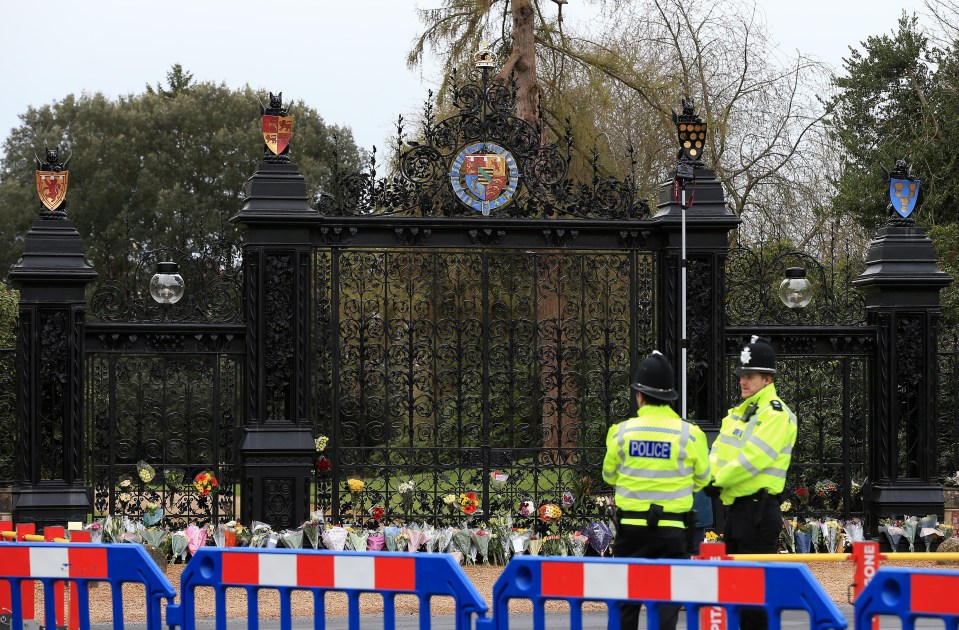Police officers patrol a closed road near to where flowers have been placed at the gates of Sandringham House