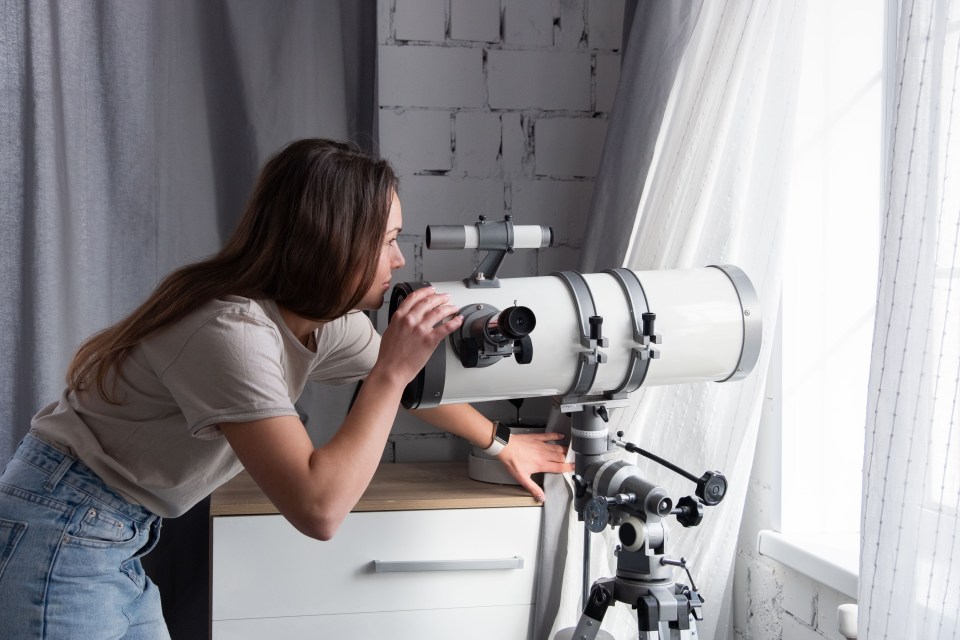 woman looking through a telescope in her bedroom