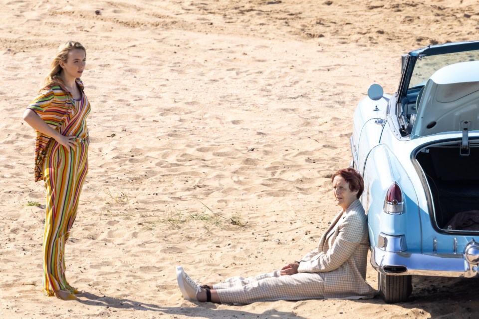 Fiona plays Carolyn and sat on the sand leaning up against a blue convertible