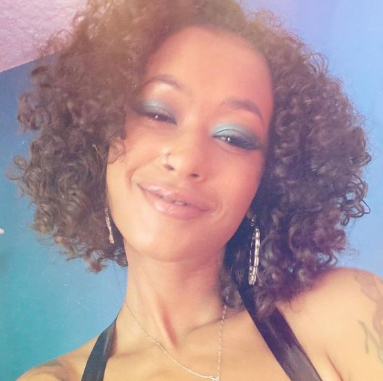 a woman with curly hair and blue eyeshadow is smiling for the camera .