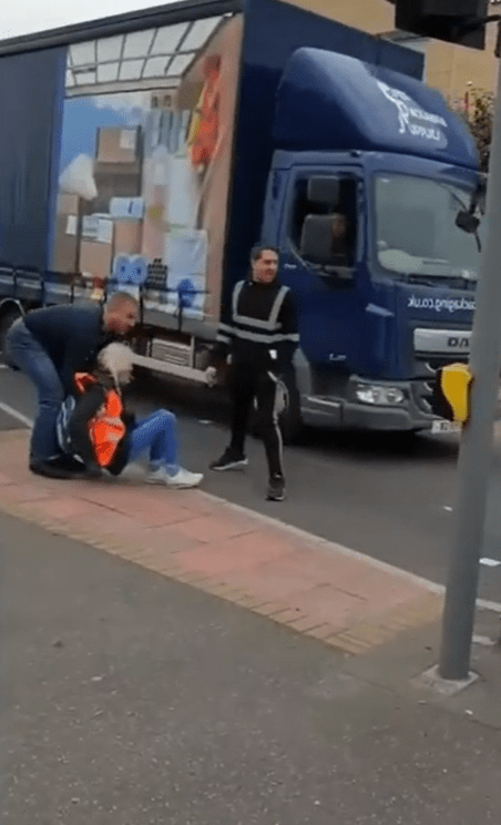 A woman with grey hair can also be seen being dragged off as a lorry rolls past