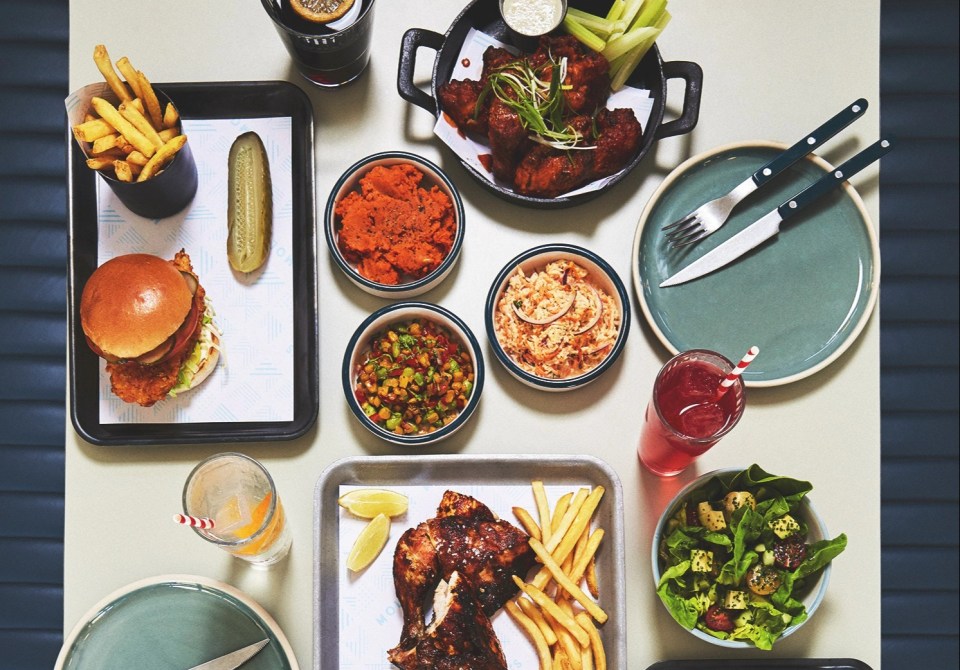 Overhead view of a table with various food items, including a chicken burger, fries, chicken wings, and a roast chicken.