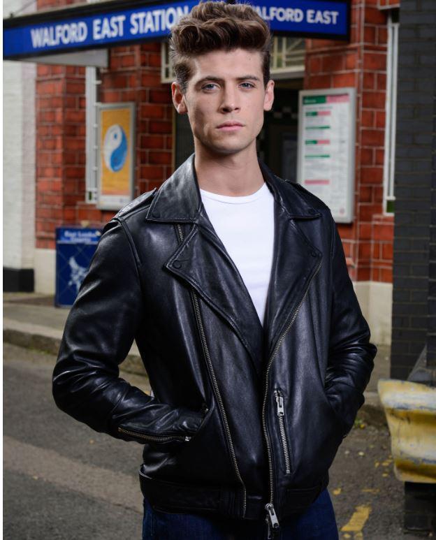 Man in black leather jacket standing outside Walford East Station.
