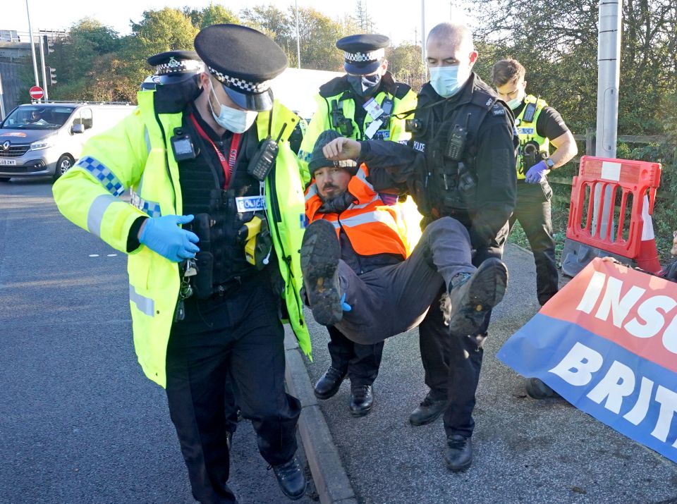 Police officers detain an activist, not necessarily one of the 74 charged, at an Insulate Britain roadblock on the M25